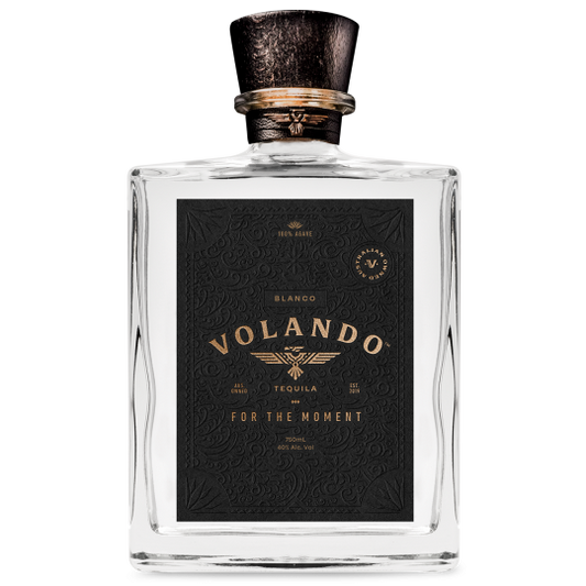 Bottle of Paramount Volando Tequila Blanco 750mL with clear glass and white label on a wooden surface.